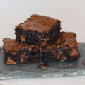 Three fudgy brownies stacked on a slate serving board