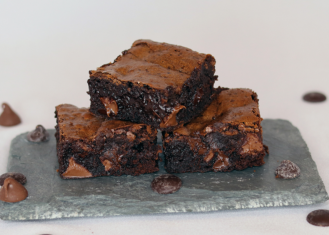 Three fudgy brownies stacked on a slate serving board