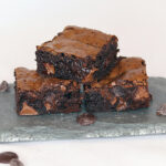 Three fudgy brownies stacked on a slate serving board