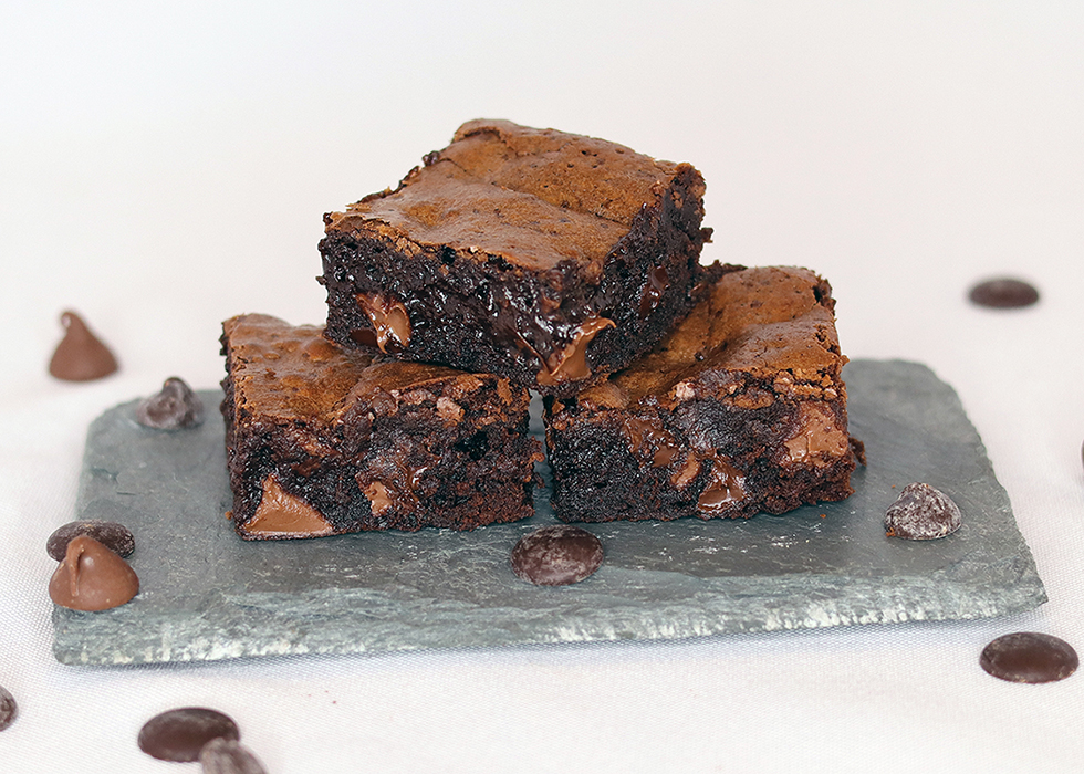 Three fudgy brownies stacked on a slate serving board