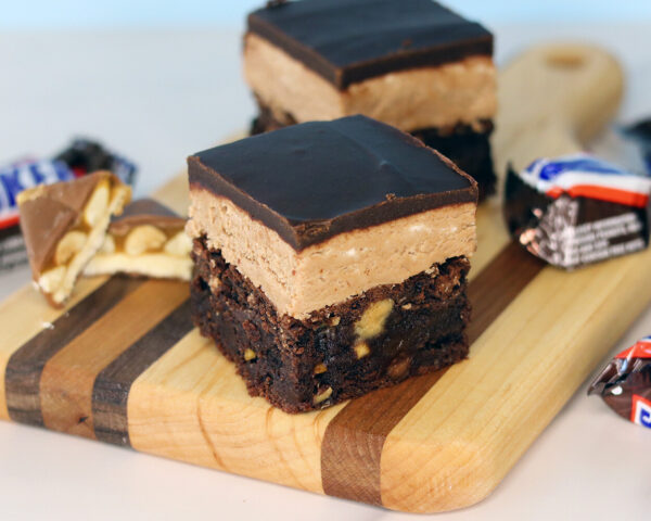 Snickers brownies on a small wooden board, showcasing the distinct layers.