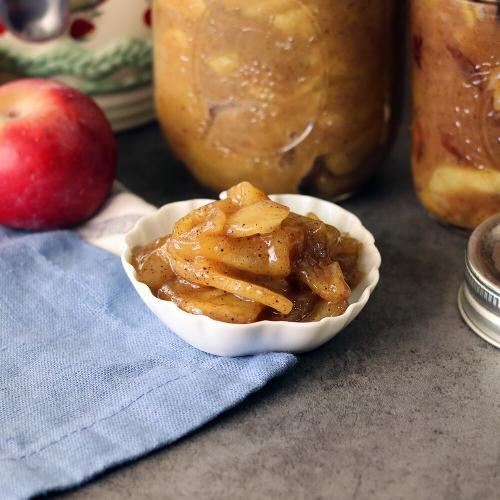 Apple Pie Filling in a small dish in front of jars of filling and apples