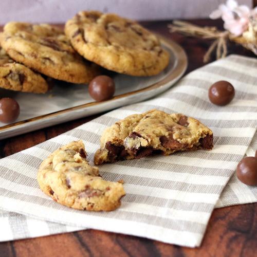 Malted Milk Chocolate Chip Cookies on a tray, one broken open in the foreground.