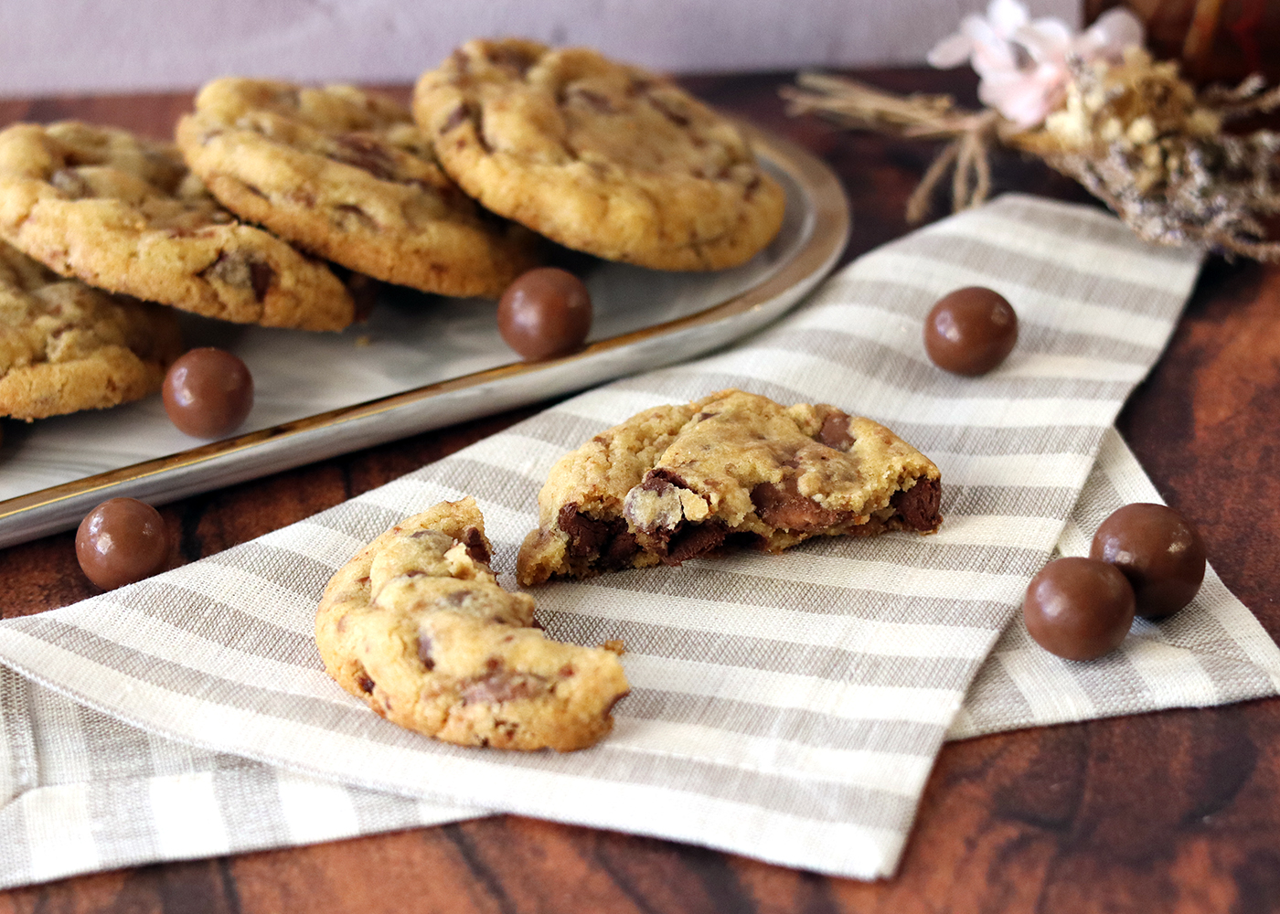 Malted Milk Chocolate Chip Cookies on a tray, one broken open in the foreground.
