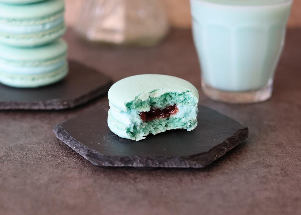 A Mandalorian Macaron on a black hexagonal plate with a bite exposing the raspberry and buttercream fillings.