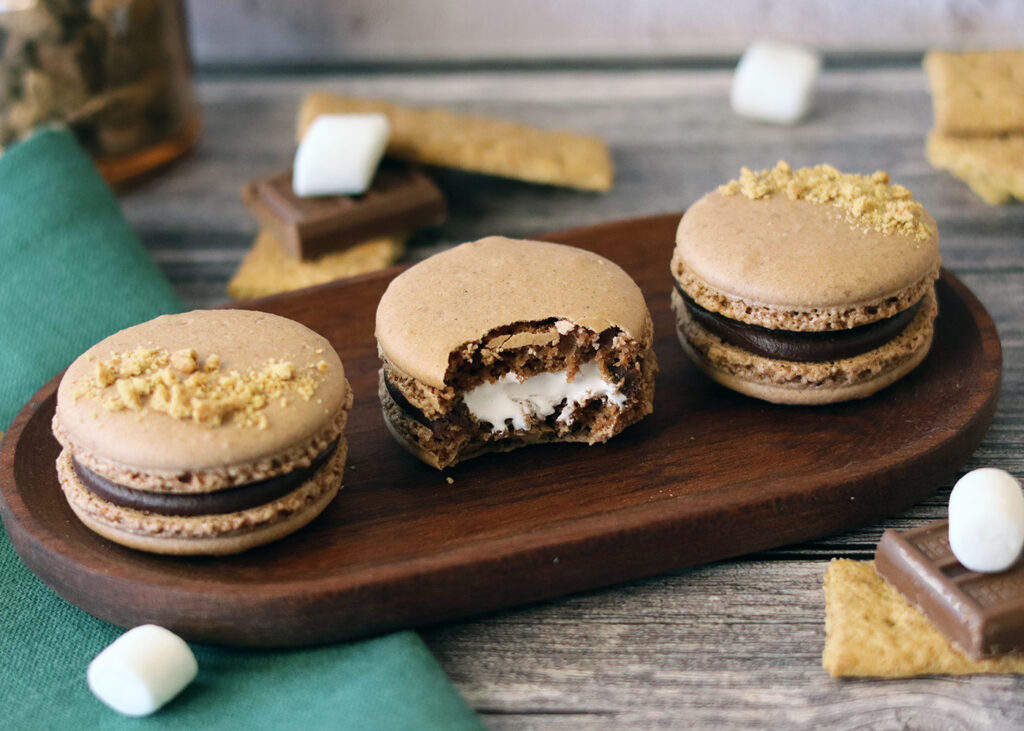 S'mores Macarons on an oblong wooden plate with a bite out of the center macaron