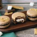 S'mores Macarons on an oblong wooden plate with a bite out of the center macaron