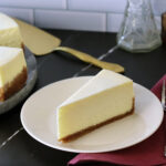 A plain slice of New York Cheesecake on a white plate.
