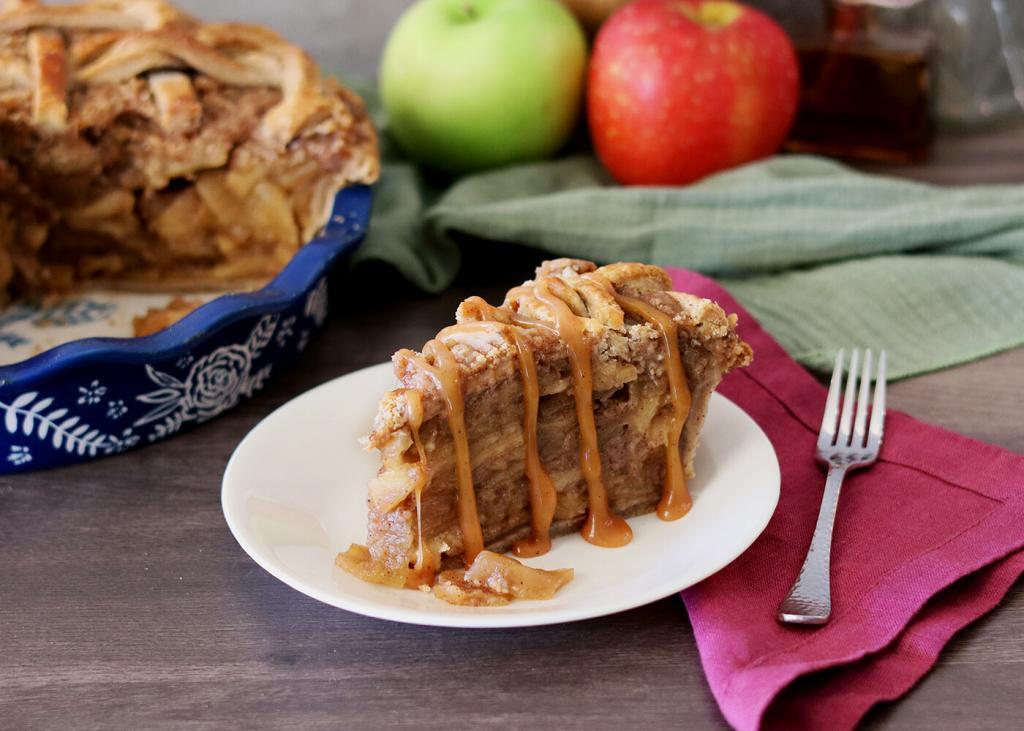 A slice of Caramel Toffee Apple Pie on a white plate drizzled with caramel.