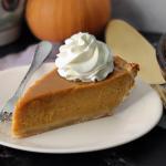 Slice of pumpkin pie topped with whipped cream on a white plate