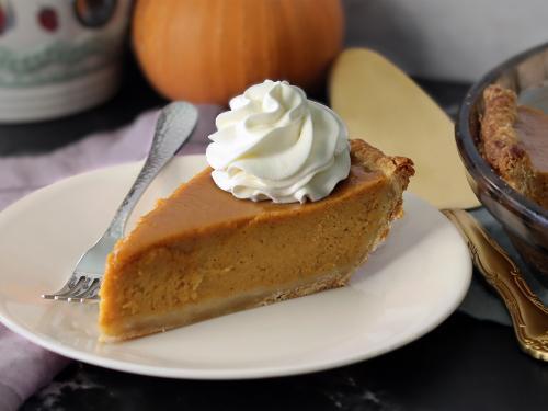 Slice of pumpkin pie topped with whipped cream on a white plate