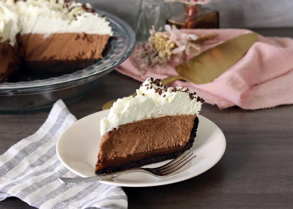 French Silk pie slice on a plate, whole pie and server in the background.