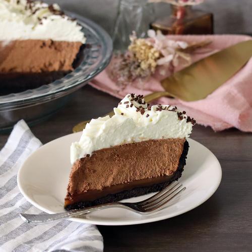French Silk pie slice on a plate, whole pie and server in the background.