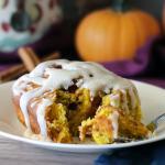 A glazed pumpkin breakfast roll with a bite cut out of it revealing layered interior
