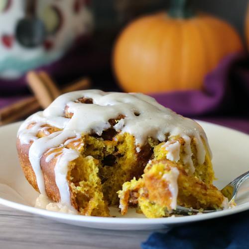 A glazed pumpkin breakfast roll with a bite cut out of it revealing layered interior