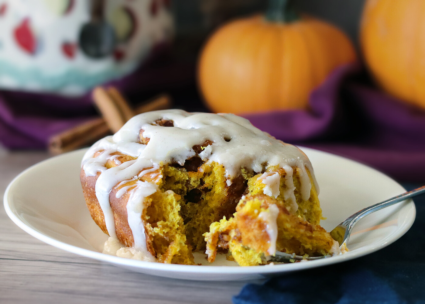 Pumpkin cinnamon roll cut open on a white plate; pumpkin jar and cinnamon sticks in the background.