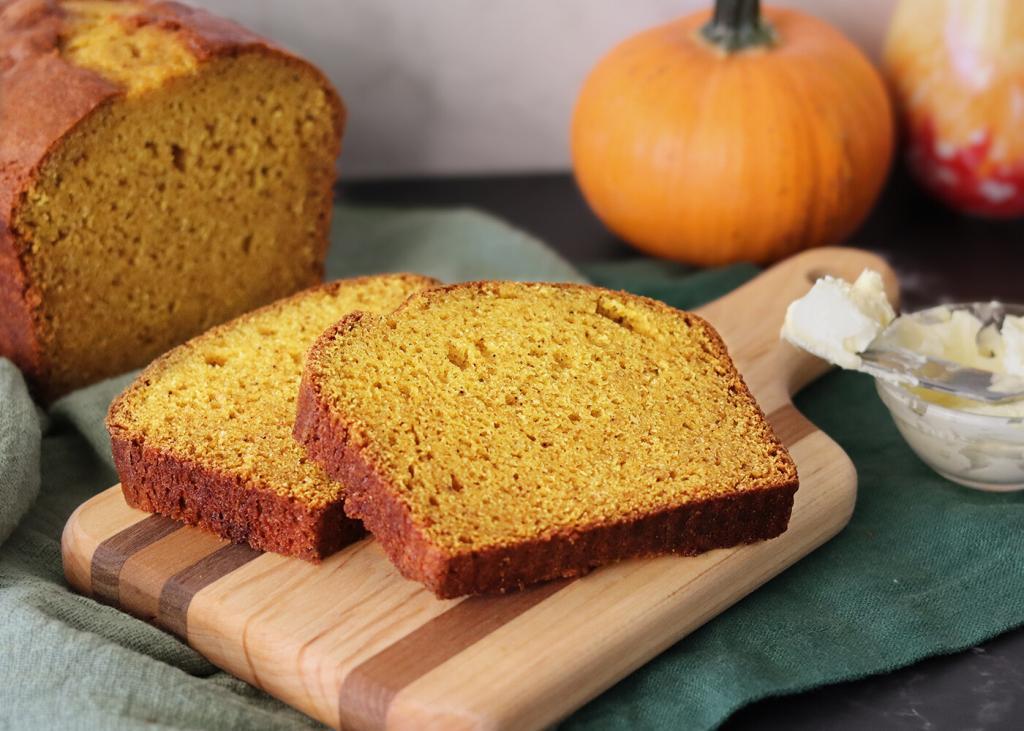 Mom's Pumpkin Bread sliced on a cutting board with a pumpkin in the background