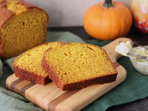 Mom's Pumpkin Bread sliced on a cutting board with a pumpkin in the background