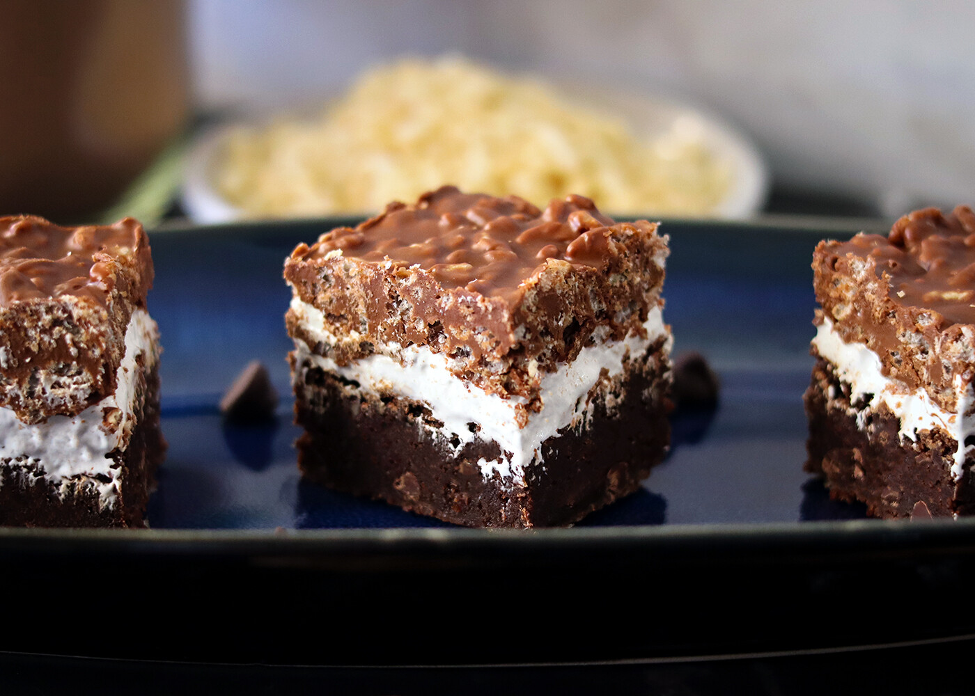 A chocolate crunch brownie on a blue platter showing distinct brownie, marshmallow and crunch layers