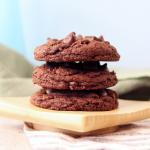 Side angle view of a stack of Double Chocolate Chip Sourdough Cookies on a small wooden board