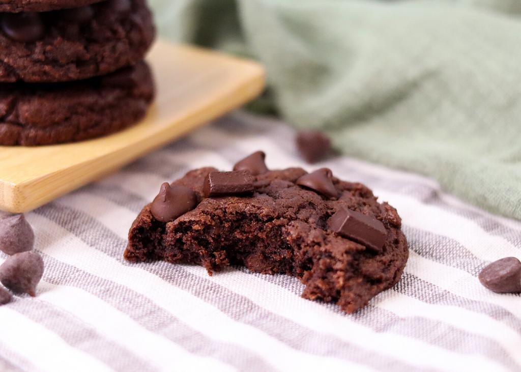 A Double Chocolate Chip Sourdough Cookie on a striped linen napkin with a large bite taken from it showing the interior.