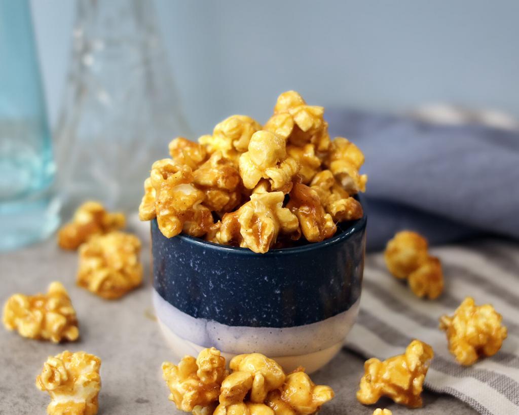 Glossy caramel popcorn in a small bowl and scattered on the table.