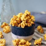 Glossy caramel popcorn in a small bowl and scattered on the table.