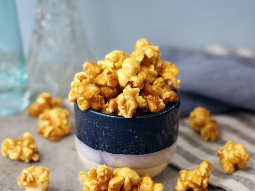 Glossy caramel popcorn in a small bowl and scattered on the table.