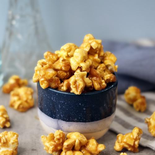 Glossy caramel popcorn in a small bowl and scattered on the table.