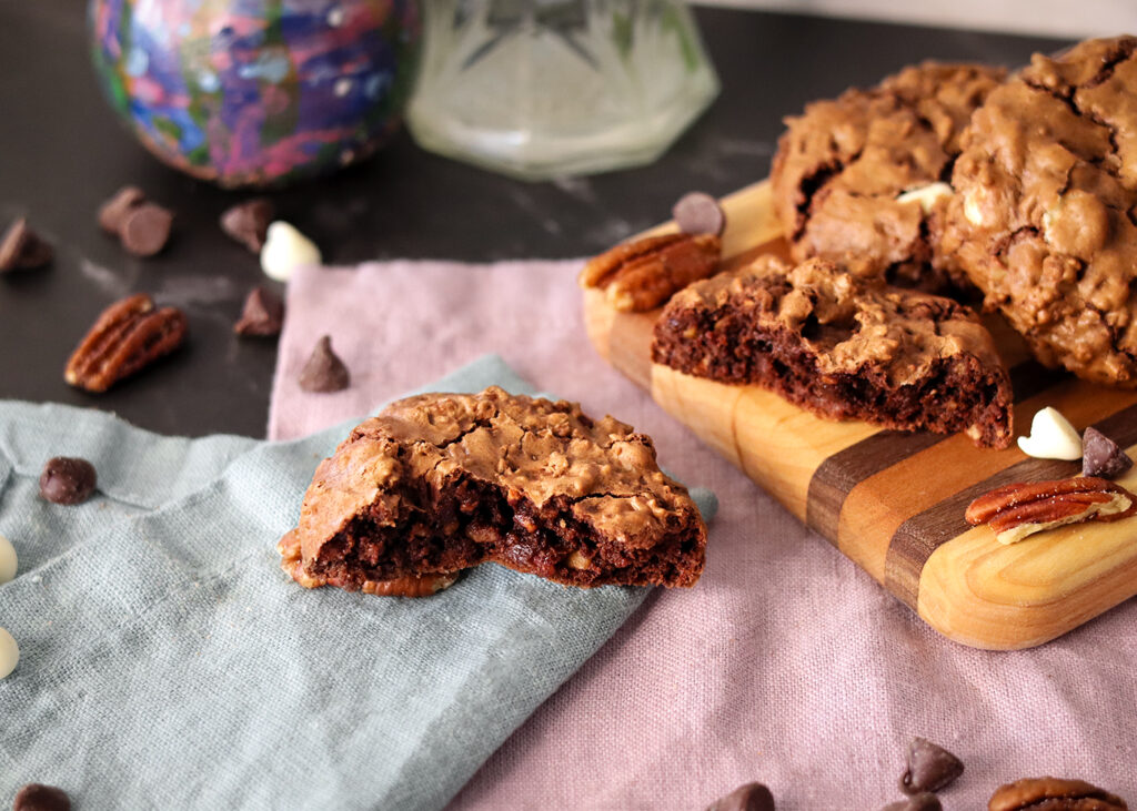 Chocolate Bliss Cookie broken to show interior texture on napkins in front of a serving board with more cookies.