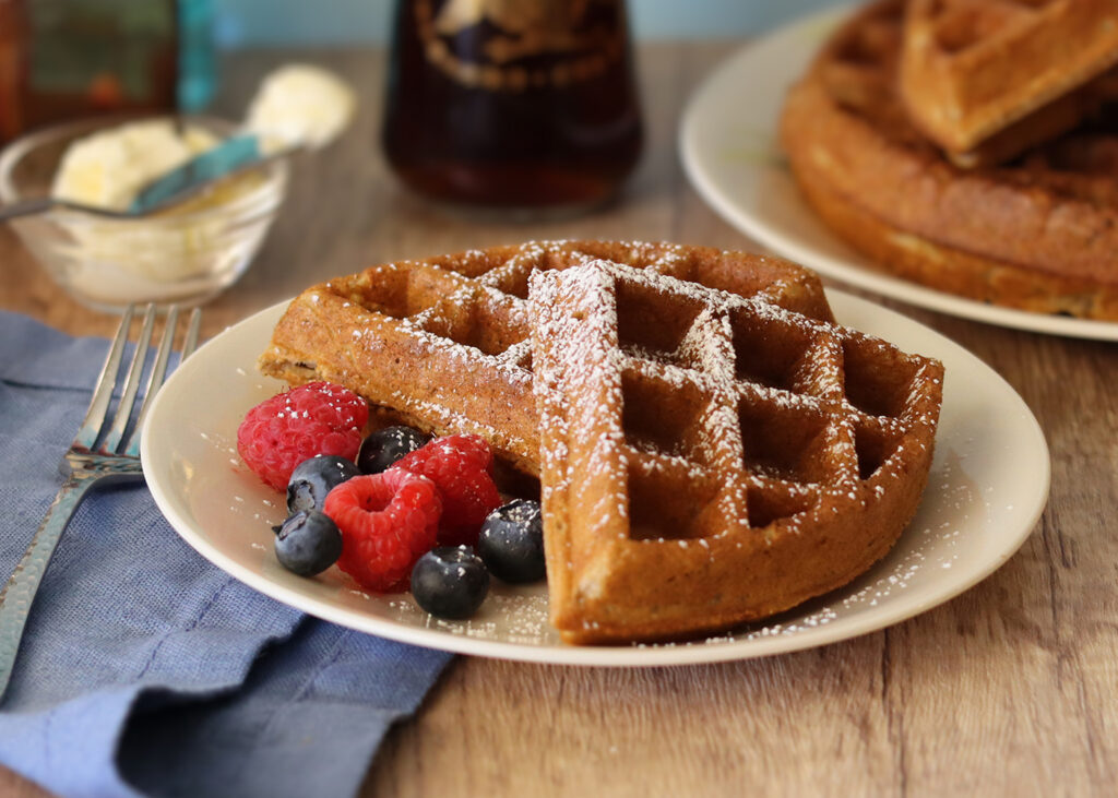 Sourdough discard waffle sections served on a white plate with fresh berries and powdered sugar.