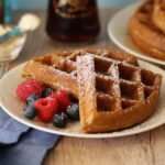 Sourdough discard waffle sections served on a white plate with fresh berries and powdered sugar.
