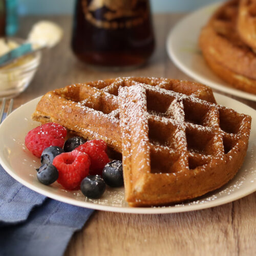Sourdough discard waffle sections served on a white plate with fresh berries and powdered sugar.
