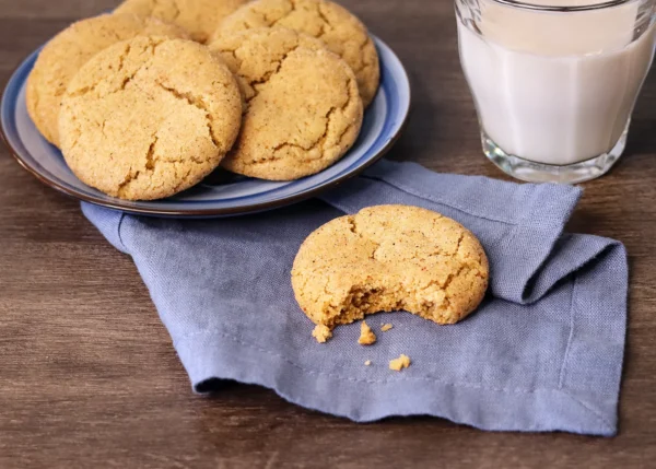 Sourdough Snickerdoodle with a bite missing showing interior texture in front of a plate of snickerdoodles.