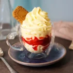 A glass cup of cheesecake mousse with a clearly visible layer of macerated strawberries and a cookie garnish.