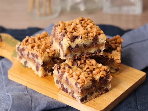 Chocolate Chip Toffee Bars stacked on a small cutting board showing the texture of the layers and toppings.