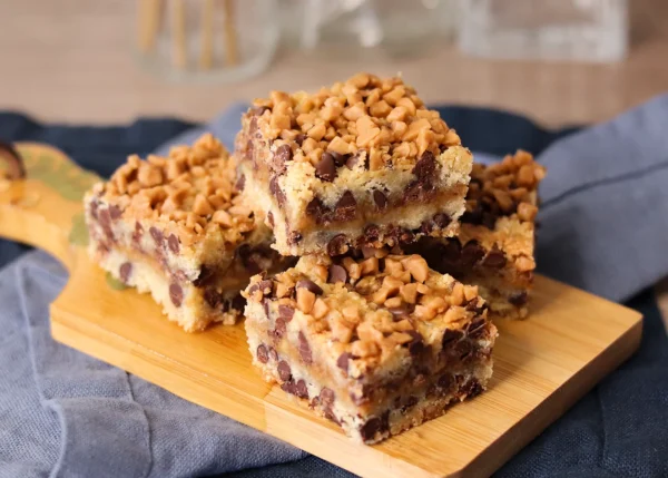 Chocolate Chip Toffee Bars stacked on a small cutting board showing the texture of the layers and toppings.