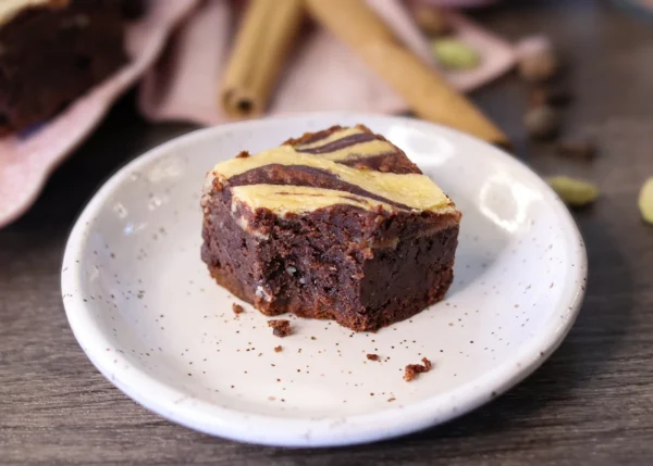 A Dirty Chai Cheesecake Brownie on a small plate with a bite taken to show the fudgy interior.