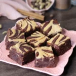 Dirty Chai Cheesecake Brownies arranged on a square pink plate and showcasing the cheesecake swirl.