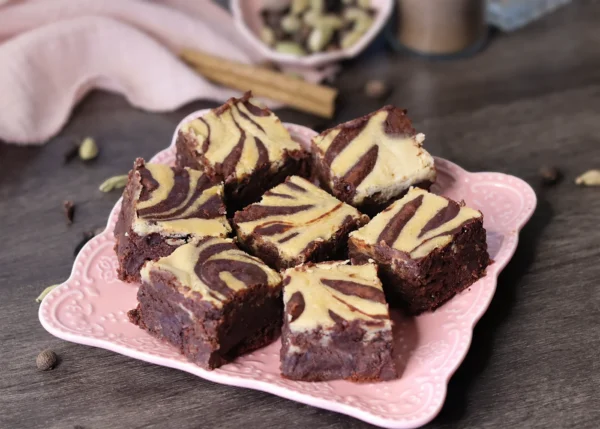 Dirty Chai Cheesecake Brownies arranged on a square pink plate and showcasing the cheesecake swirl.